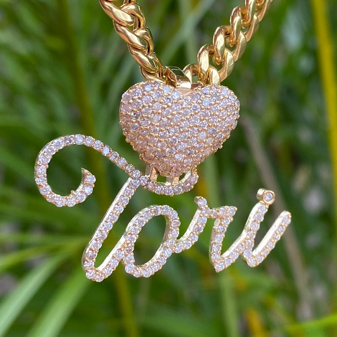 A gold-colored heart-shaped pendant with a customized name 'Tori' written in cursive script, adorned with diamonds.